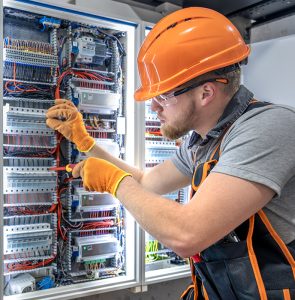 Male electrician working in electrical panel. Male electrician in uniform. High quality photo. Male construction worker in helmet and safety glasses. Copy space.
